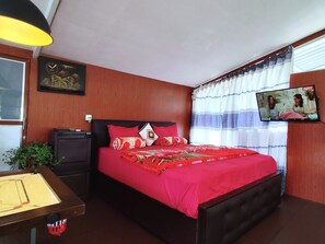 A bedroom with a bed, a TV, a desk with a board game, and a window with curtains.