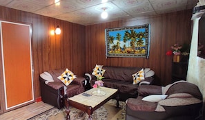 Un salon avec un ensemble de canapés marron, une table basse et un tableau représentant un paysage tropical, accroché au mur.