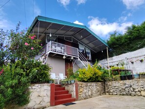 A house with a balcony, a stone wall, and a staircase leading to the entrance.