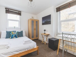A bedroom with a bed, a wardrobe, a desk, and a window with a view of a brick wall. - Bright Loft Apartment in Nine Elms (London)