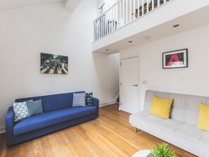 A living room with a blue sofa, a grey sofa, wooden flooring, a staircase, and a white door. - Bright Loft Apartment in Nine Elms (London)