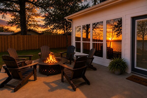 Eine Terrasse mit Adirondack-Stühlen, einer Feuerstelle und Blick auf einen Sonnenuntergang über dem Wasser.