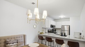 Eine moderne Küche mit weißen Schränken, einem Edelstahlkühlschrank und einem eingebauten Backofen. Es gibt eine Essecke mit einem Holztisch und vier Stühlen.