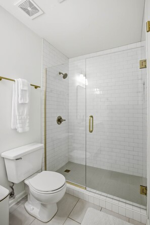 Ein Badezimmer mit Toilette, einer gläsernen Dusche und einer weißen Fliesenwand.