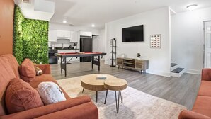 Una sala de estar con mesa de billar, sofá, mesa de centro y televisor montado en la pared.