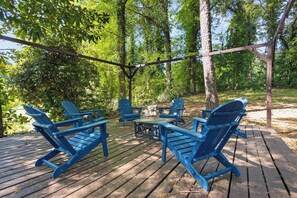 A wooden deck with blue Adirondack chairs and a small table, surrounded by trees.
