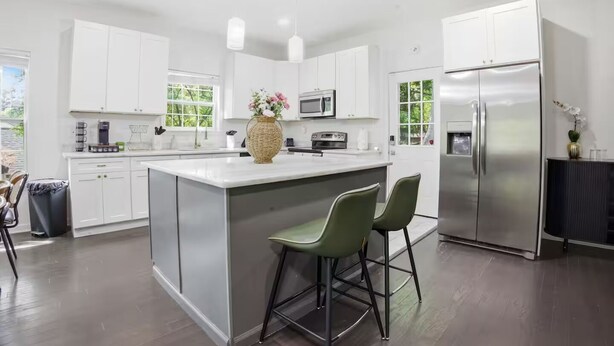 Una cocina moderna con armarios blancos, un refrigerador de acero inoxidable y una isla central con taburetes de bar.