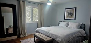 Una camera da letto con un letto, una panca, un comodino, un quadro incorniciato e una finestra con tende.