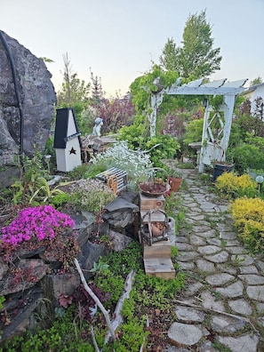 Ein Gartenweg mit einem Willkommensschild, einer hölzernen Bank und einer Pergola.