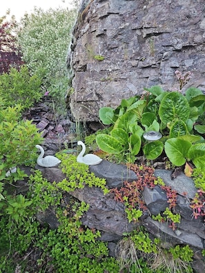 A garden with a rock wall, green plants, and two swan sculptures.