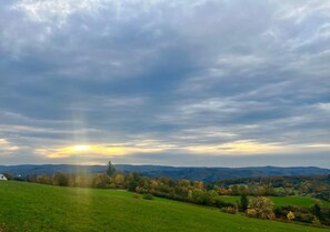 A landscape with a house on a hill, green fields, and distant mountains. - Climate-Friendly Vacation Home in the Eifel – Near the Nürburgring & the Ahr Wine Region (Lind)