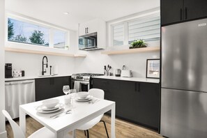 Eine moderne Küche mit weißen Schränken, einem Edelstahlkühlschrank und einem Essbereich mit weißem Tisch und Stühlen.