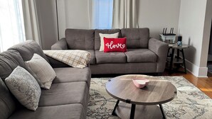 En stue med sofa, sofabord, lampe og et vindue med gardiner.