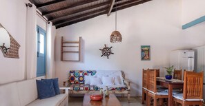 A living room with a sofa, a dining table with chairs, a ladder, a ceiling fan, and a refrigerator. - Casa Cond. Outeiro das Brisas PS - BA (Porto Seguro)