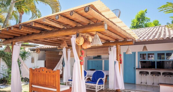 A wooden pergola with hanging lights, a blue chair, and a bar area with stools.
