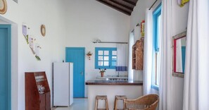 A kitchen with a blue door, a refrigerator, a sink, and a window with a curtain. - Casa Cond. Outeiro das Brisas PS - BA (Porto Seguro)
