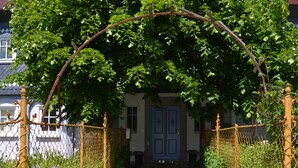 A stone pathway leading to a house with a blue door, surrounded by a yellow fence and greenery.