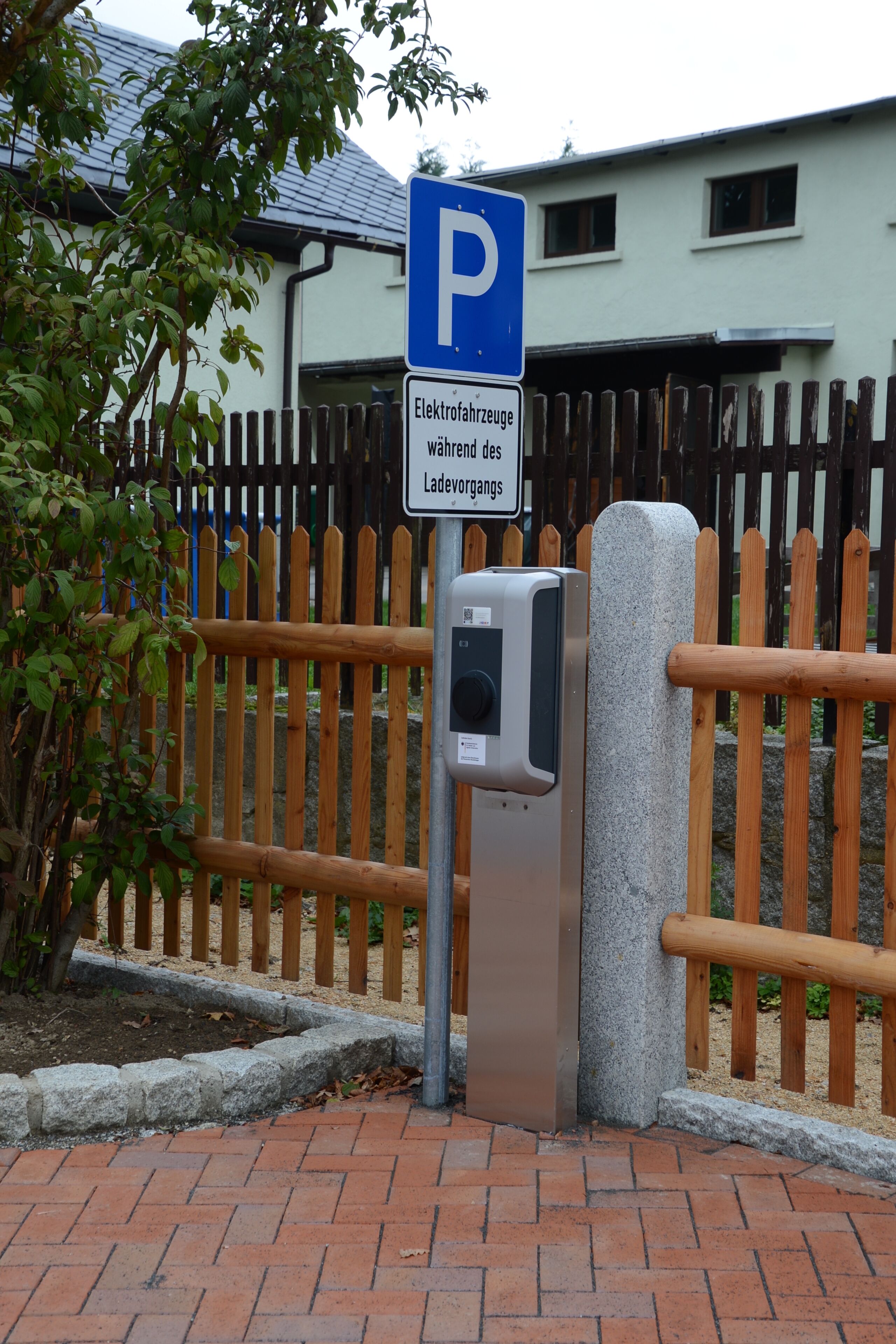 A parking sign with a metal barrier and a stone pillar.