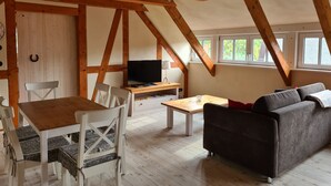 A loft-style room with wooden beams, a TV, a sofa, a dining table, and chairs.