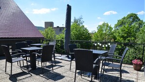 An outdoor patio with tables and chairs, a potted plant, and a building with a red roof in the background.