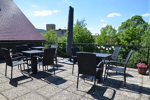 En uteplats med bord och stolar, en krukväxt och en byggnad med ett rött tak i bakgrunden.