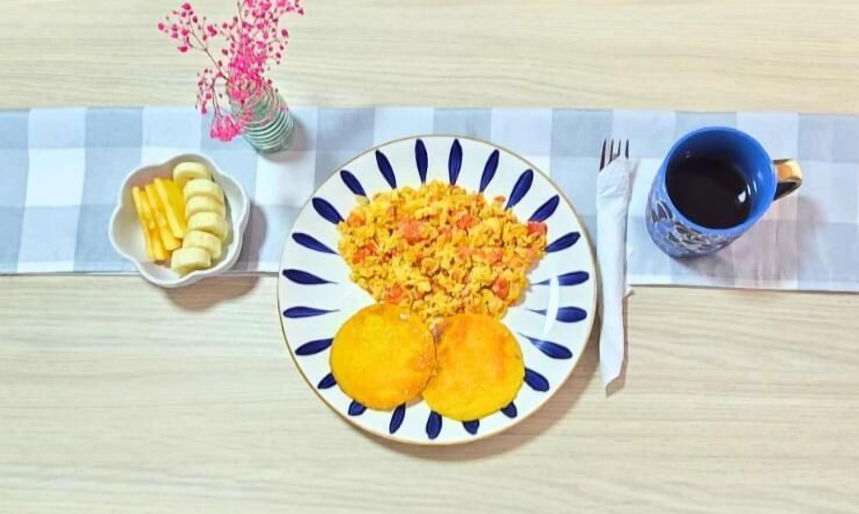 A plate of food with a blue and white pattern, a blue cup, and a small bowl of bananas on a checkered tablecloth.