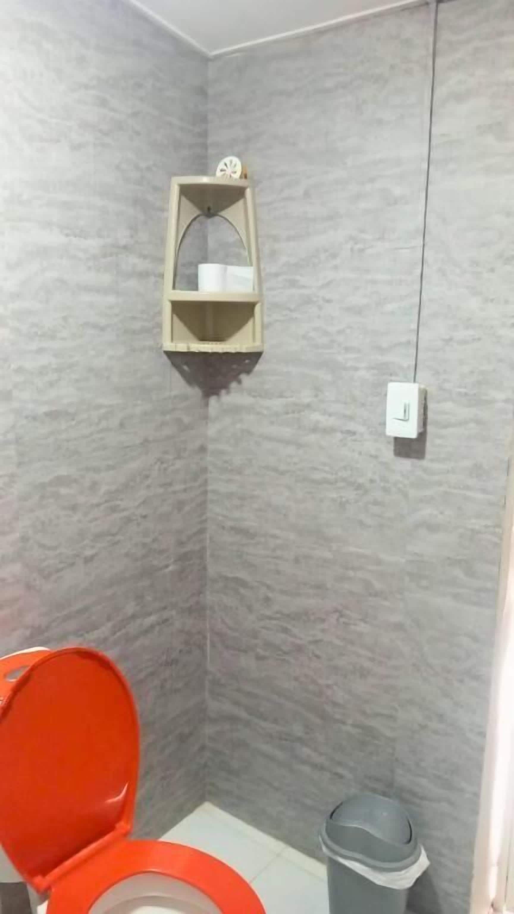Un baño con un inodoro, un estante con artículos de aseo y un cubo de basura.