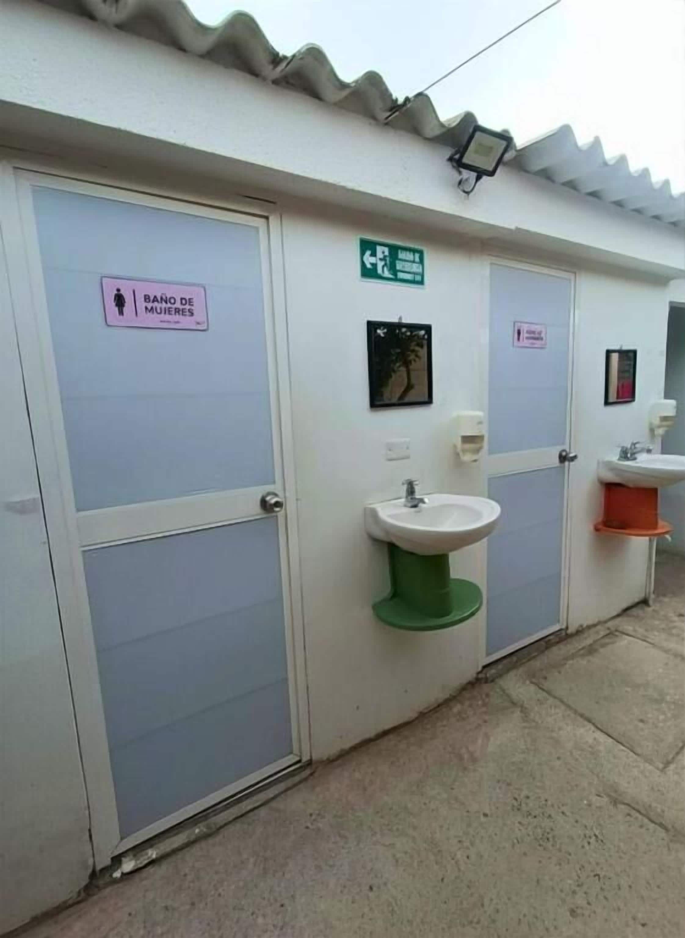 Baño de mujeres con un letrero, un indicador direccional verde y un lavamanos.