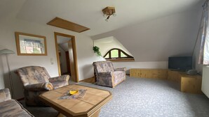 Habitación estilo loft con techo alto, una viga de madera, televisor, sofá, mesa de centro y ventana con vistas.