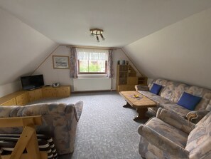 A loft-style room with a sofa, armchair, and a television on a wooden cabinet.