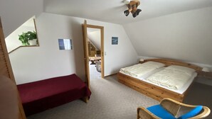 Un dormitorio con una cama individual, una silla, un ventilador de techo de madera y una planta pequeña.