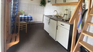 Una cocina con armarios de madera, una mesa de comedor con sillas, un reloj en la pared y una planta.