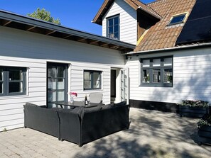 Un edificio bianco con una zona patio, un tavolo in vimini nero e una sedia.