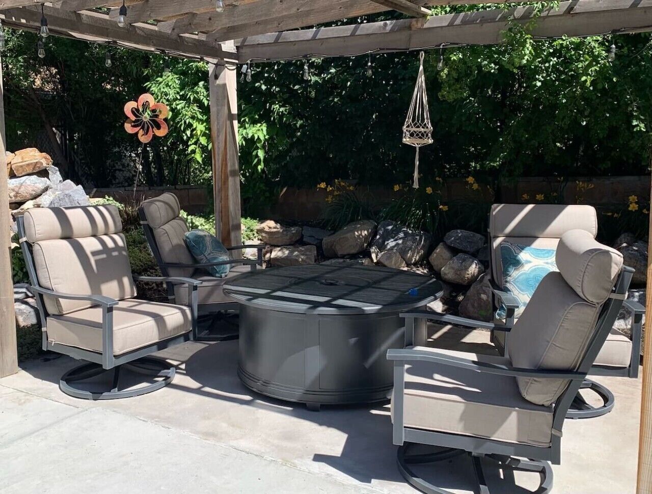 Une terrasse extérieure avec une table ronde et quatre chaises, entourée d’une pergola et d’un mur en pierre.