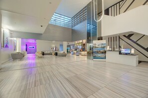 Eine großzügige Lobby mit hoher Decke, einer Sitzecke mit Sofas, einem Empfangstisch und einer Treppe.