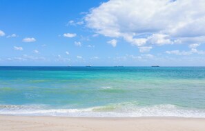 Ein Strand mit klarem türkisblauem Wasser, einem Sandufer und ein paar Schiffen in der Ferne.