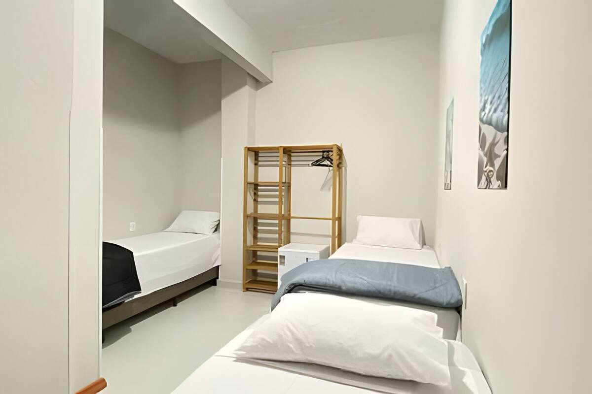 Une chambre de taille modeste, équipée de deux lits simples, d’une armoire en bois et d’une petite table de chevet.