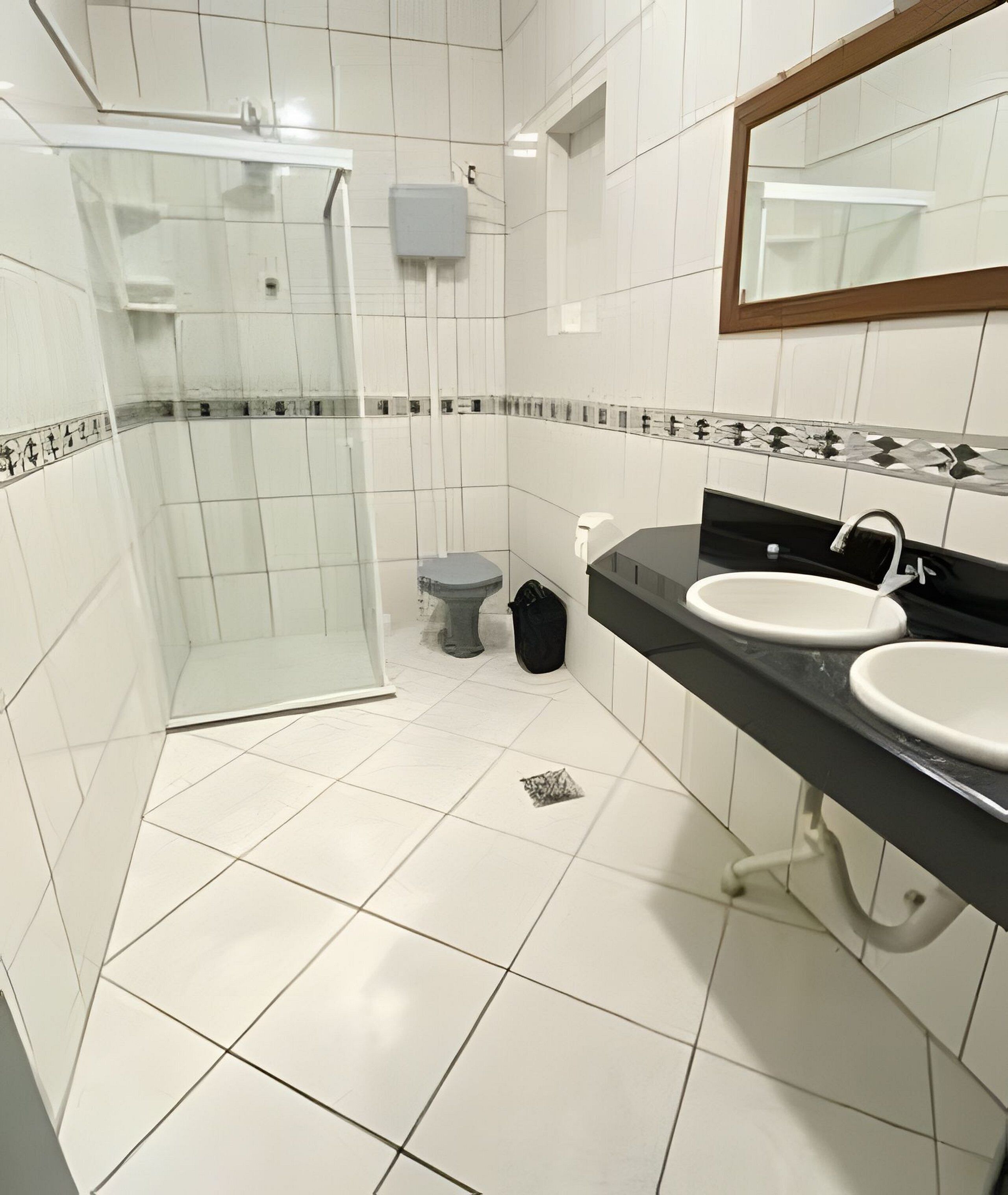 A bathroom with a glass shower enclosure, a toilet, and two sinks with black countertops.