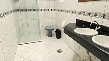 A bathroom with a glass shower enclosure, a toilet, and two sinks with black countertops.