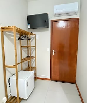 Una habitación con una estantería de madera, un electrodoméstico blanco, una puerta de madera cerrada y un aire acondicionado instalado.