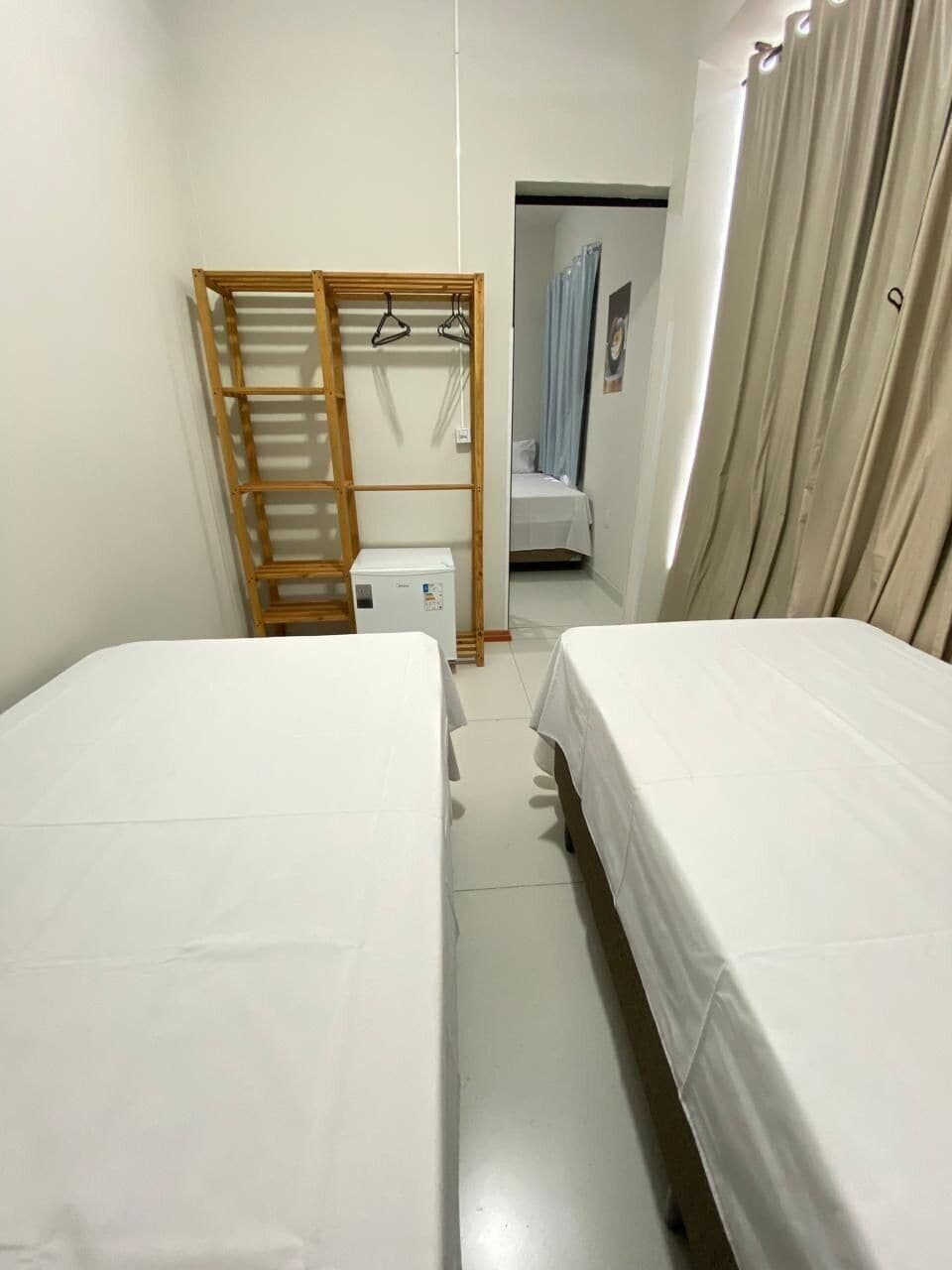 Een kleine, nette kamer met twee bedden, een houten trapje, een klein wit kastje en een deur naar een andere kamer.
