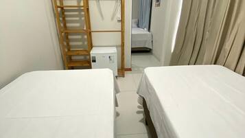 Een kleine, nette kamer met twee bedden, een houten trapje, een klein wit kastje en een deur naar een andere kamer.