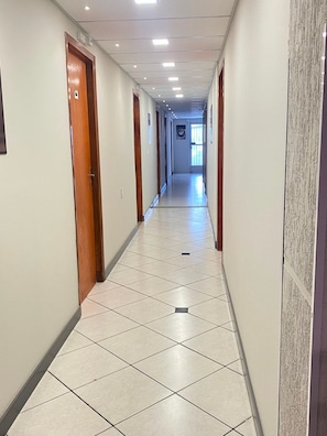 A long, narrow hallway with tiled flooring and wooden doors on both sides. - Pousada Âncora (Gravataí)