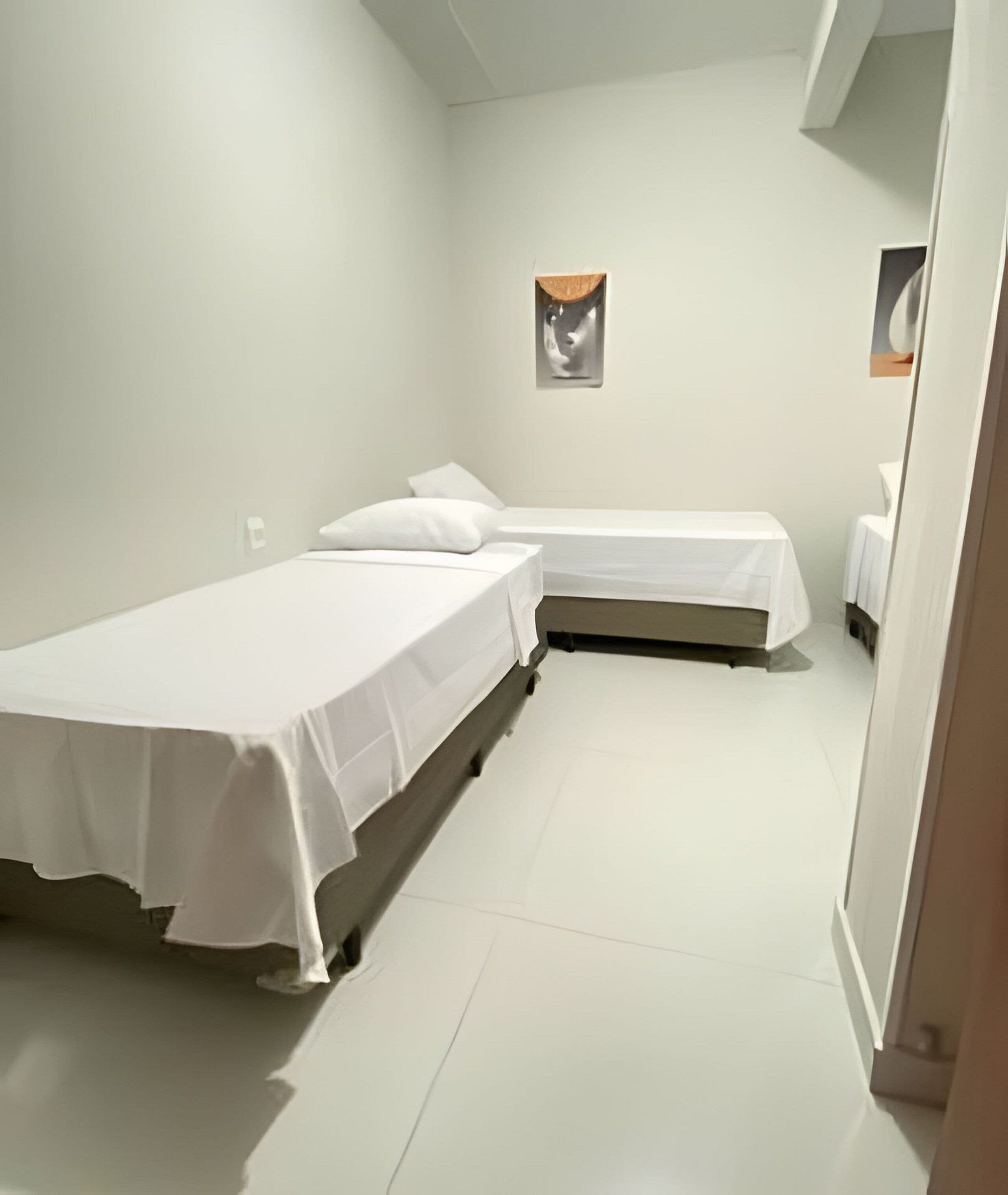 Une petite chambre propre, avec deux lits simples, des murs blancs et un aménagement simple et épuré.