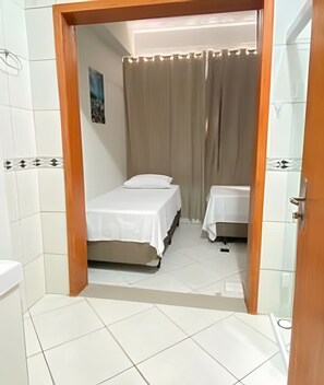 A bathroom with white tiled walls and floor, a wooden door frame, and a shower curtain. - Pousada Âncora (Gravataí)