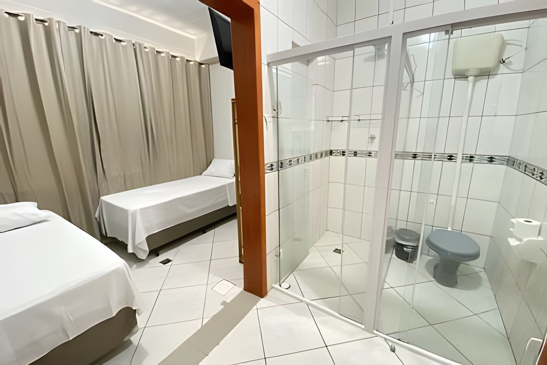 A hotel room with a bed, a shower enclosure, and a toilet.