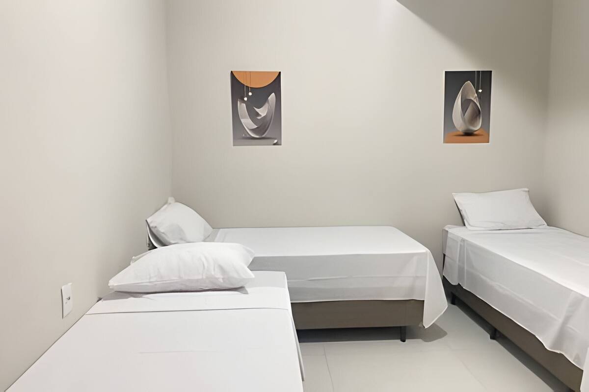 Une chambre avec deux lits simples, un mur blanc et deux tableaux encadrés.