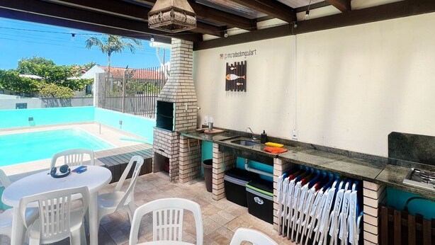 An outdoor patio with a pool, a brick oven, and a grill area. - Casa praia da pinheira Piscina (Palhoça)