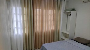 A bedroom with a bed, a wardrobe, and a window with curtains. - Casa praia da pinheira Piscina (Palhoça)