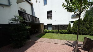 Une cour avec un chemin pavé, un petit arbre et un bâtiment doté d’un balcon.